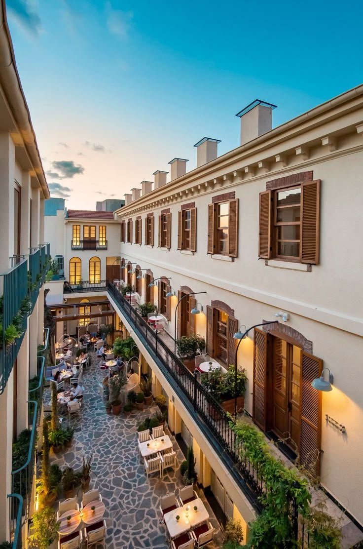 This may contain: an apartment building with tables and chairs on the balcony at dusk or dawn, overlooking a courtyard