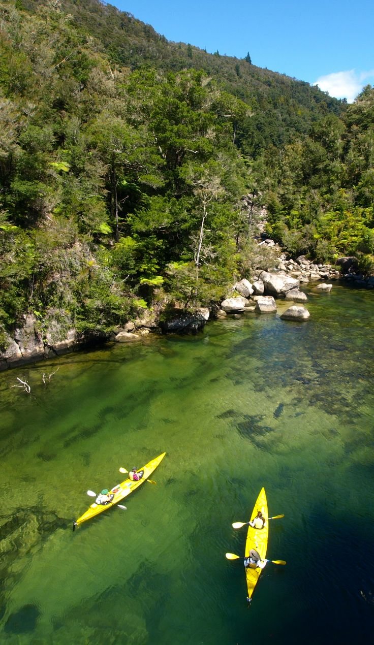 This may contain: two kayakers are in the middle of a river with clear blue water and green trees