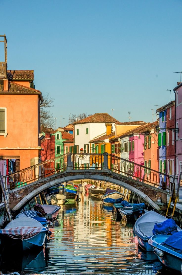 This may contain: boats are parked on the water in front of colorful buildings and a bridge over it