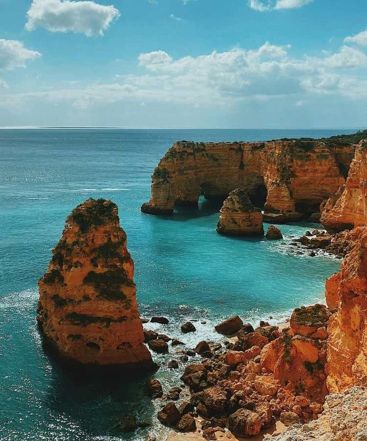 This may contain: the ocean is blue and clear with rocks on both sides as well as an arch shaped rock formation
