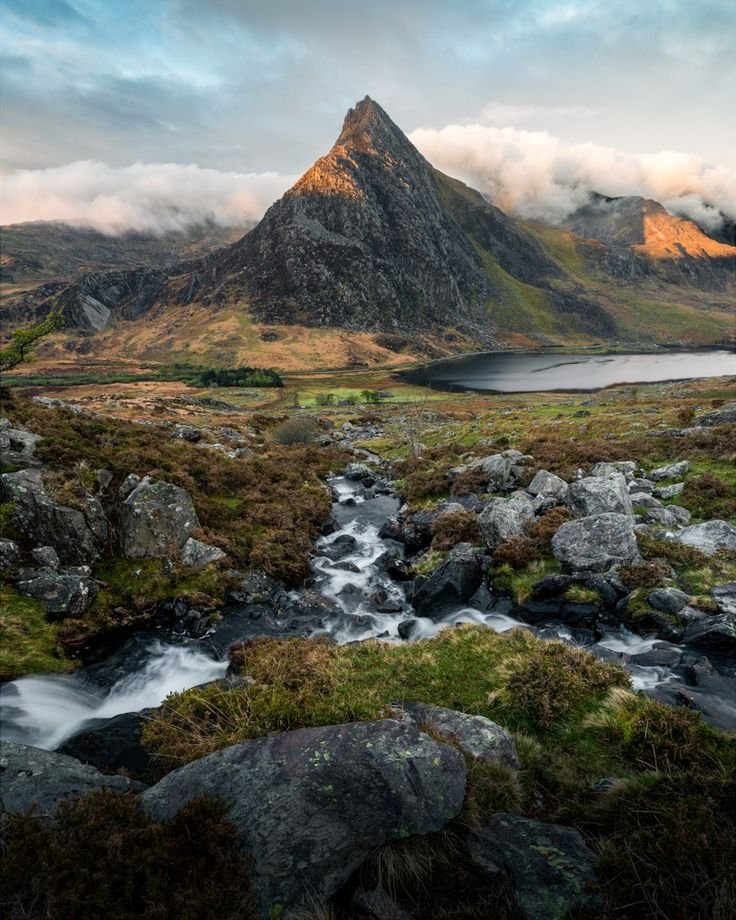This may contain: the mountains are covered in clouds and water, with small stream running between them on either side