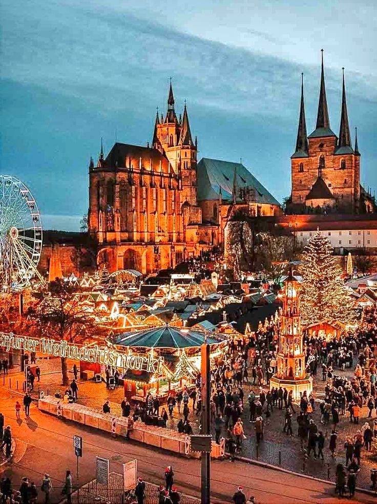 This may contain: people are walking around in front of an old castle at night with christmas lights on the ground