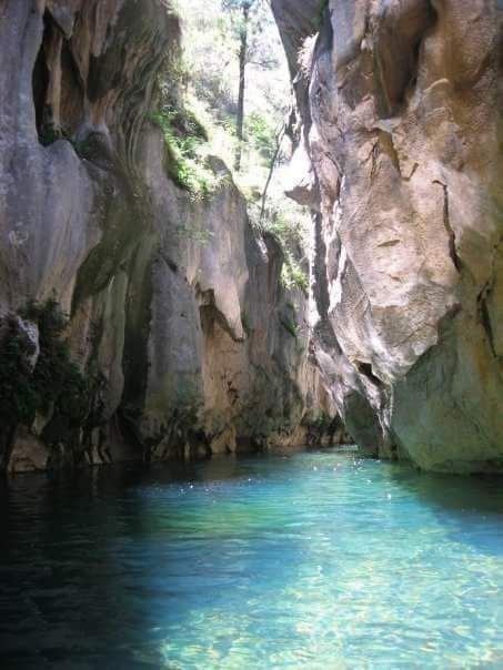 This may contain: the water is crystal blue and clear in this cave like area with cliffs on either side