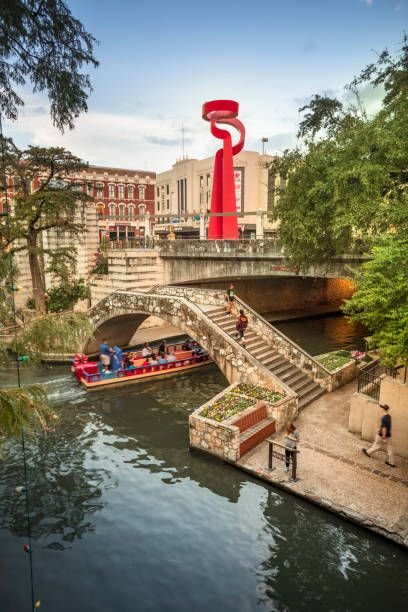 This may contain: a red sculpture on the side of a river next to a bridge and people walking