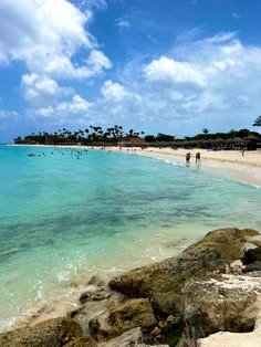 This may contain: people are swimming in the clear blue water on a beach with large rocks and palm trees