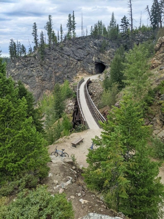 This may contain: a train going through a tunnel in the mountains with trees on both sides and benches to the side