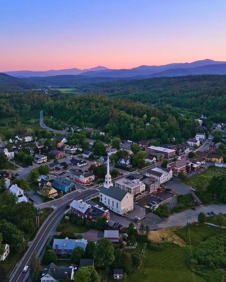 This may contain: an aerial view of a small town with mountains in the background at sunset or dawn