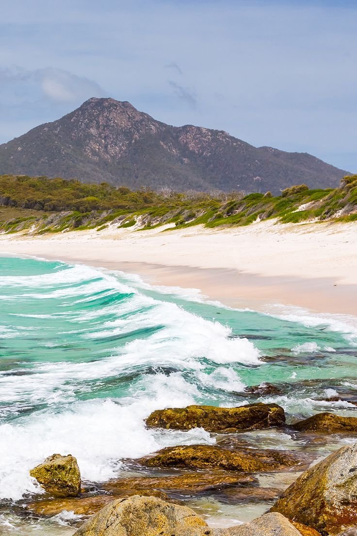 This may contain: an ocean with waves crashing on the shore and mountains in the backgrouund