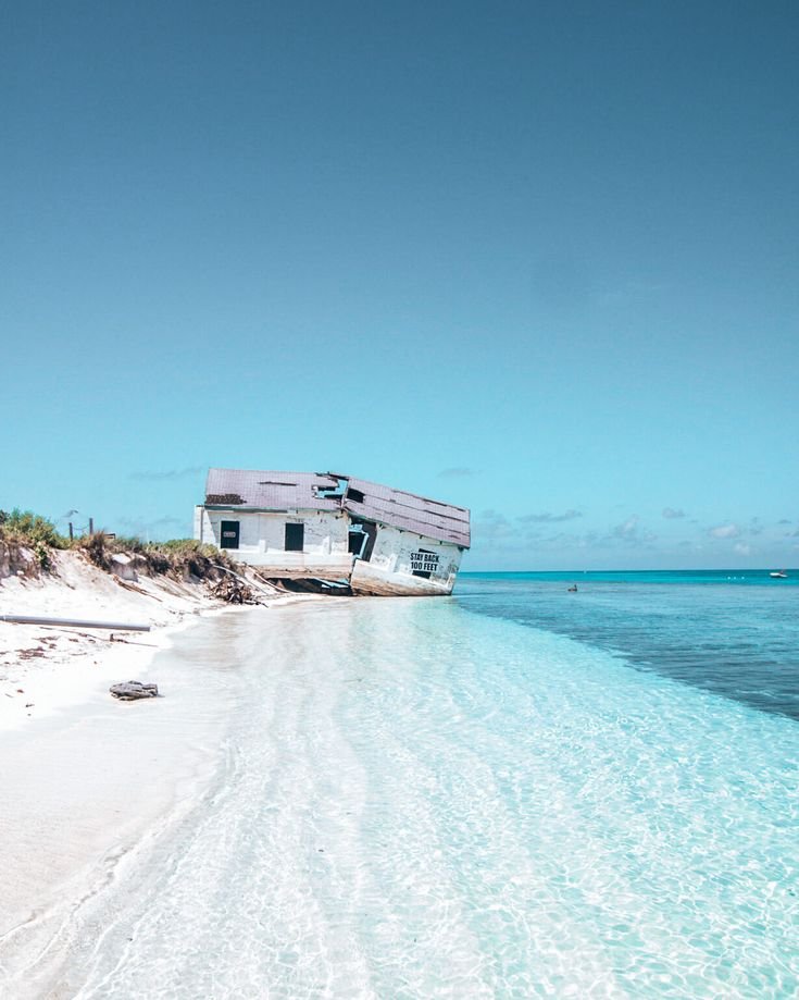 This may contain: an abandoned boat sits on the shore of a tropical beach, surrounded by clear blue water