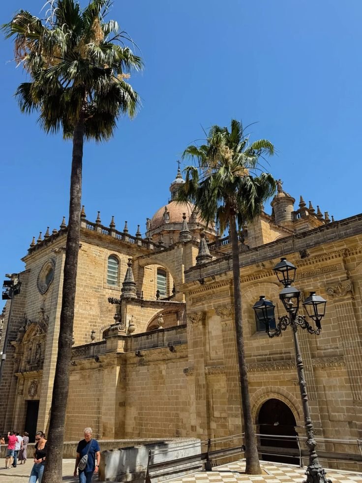 This may contain: two palm trees in front of an old building with people walking around the courtyard and on the sidewalk