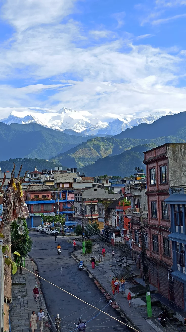 This may contain: a city with mountains in the background and people walking on the sidewalk near buildings that have been painted blue