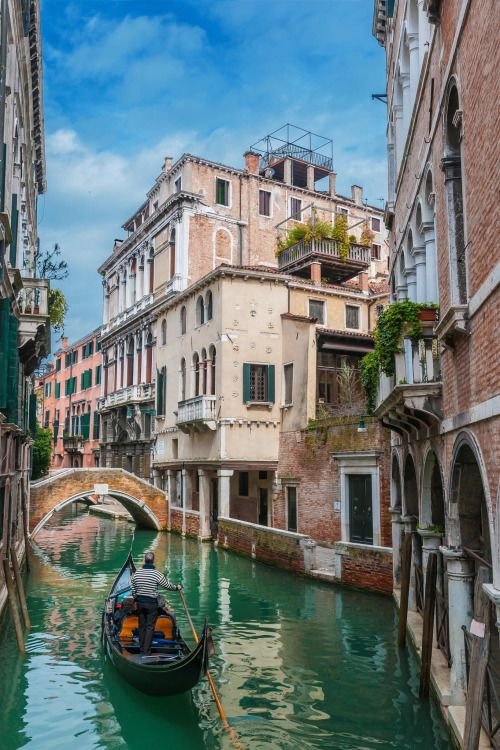 This may contain: a gondola in the middle of a narrow canal with buildings on both sides