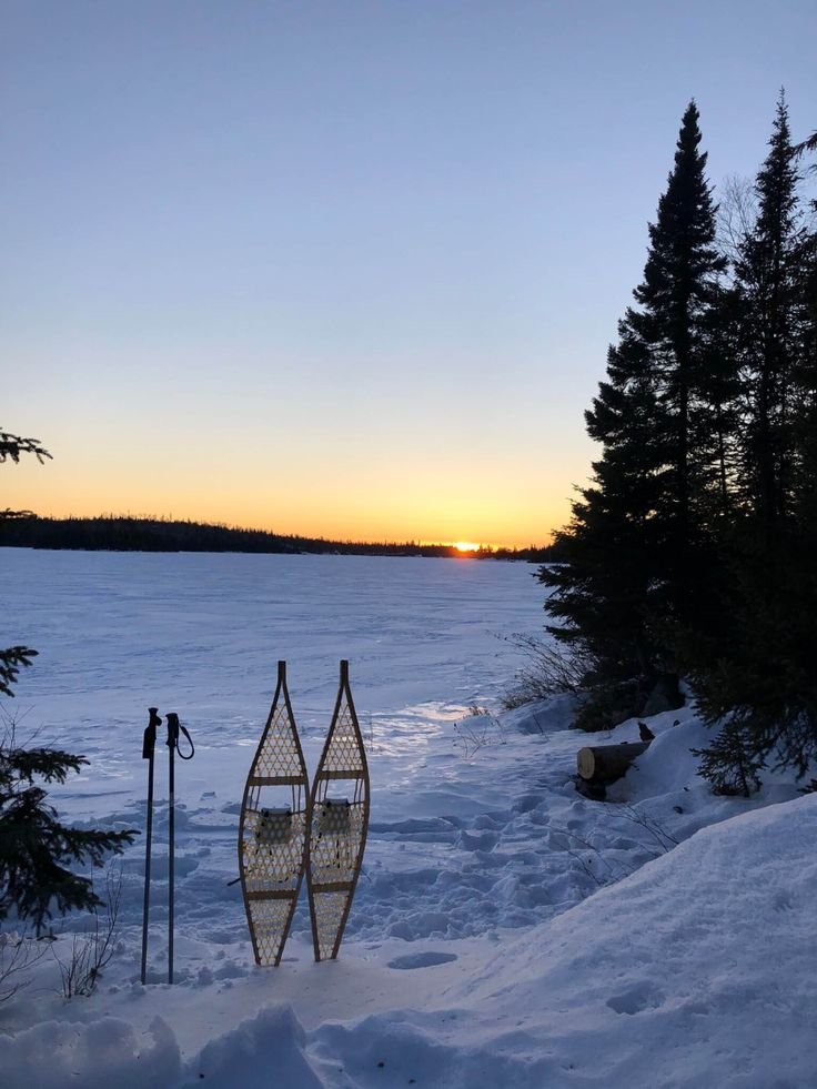 This may contain: the sun is setting behind some trees and snow covered ground with skis on it