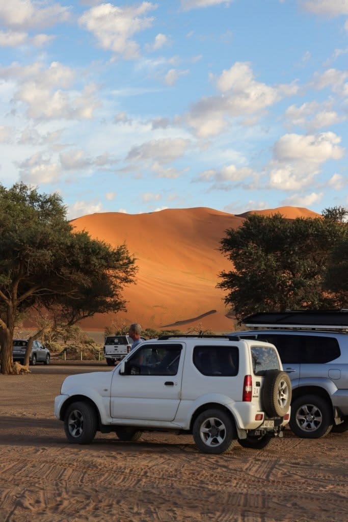 This may contain: two vehicles are parked in the dirt near trees and sand dunes with mountains in the background