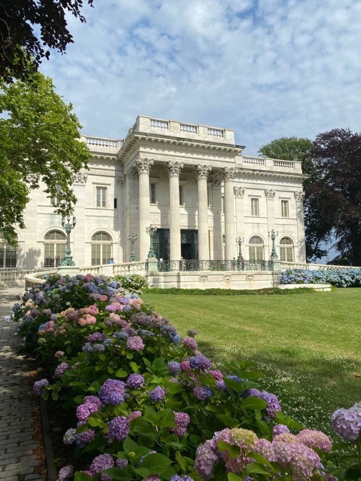 This may contain: a large white building with columns and pillars on the front, surrounded by purple flowers