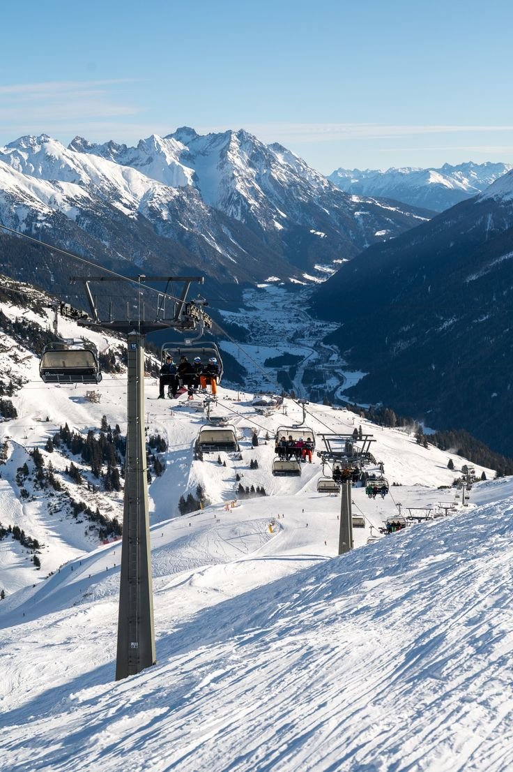 This may contain: a ski lift going up the side of a snow covered mountain with mountains in the background