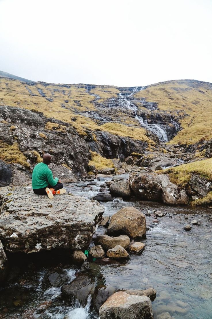 This may contain: a man sitting on top of a rock next to a river