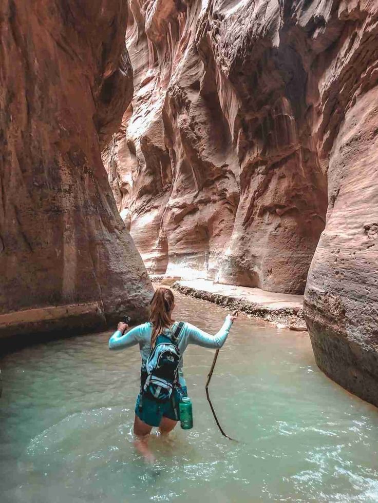 This may contain: a woman wading through the water in a canyon