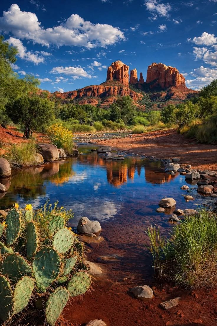 This may contain: a river running through a lush green forest next to tall red rock formations in the distance