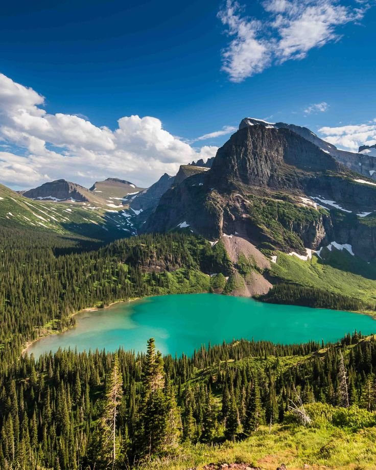 This may contain: a lake surrounded by trees and mountains under a blue sky