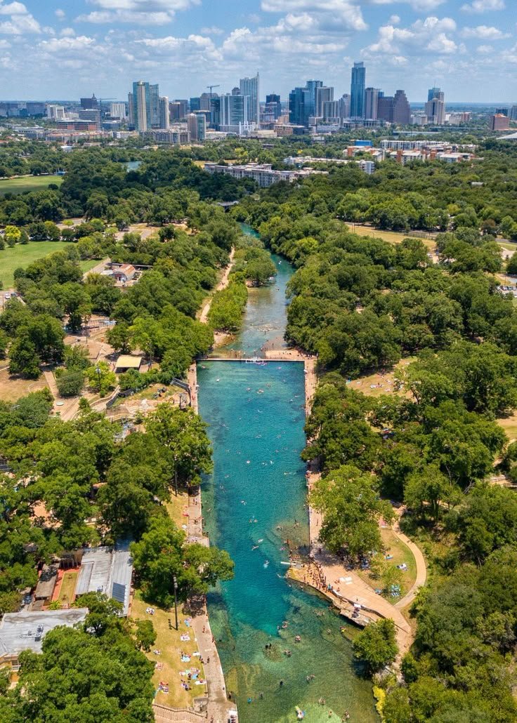 This may contain: an aerial view of a river running through a park with trees and buildings in the background