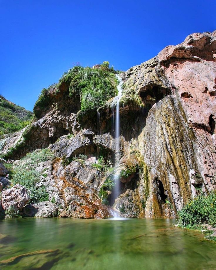 This may contain: there is a small waterfall in the middle of some rocks and green water below it