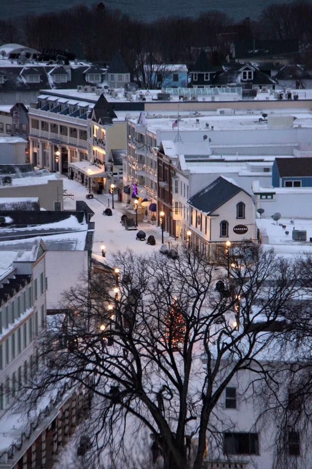 This may contain: the city is covered in snow and lit up by street lights, trees, and buildings