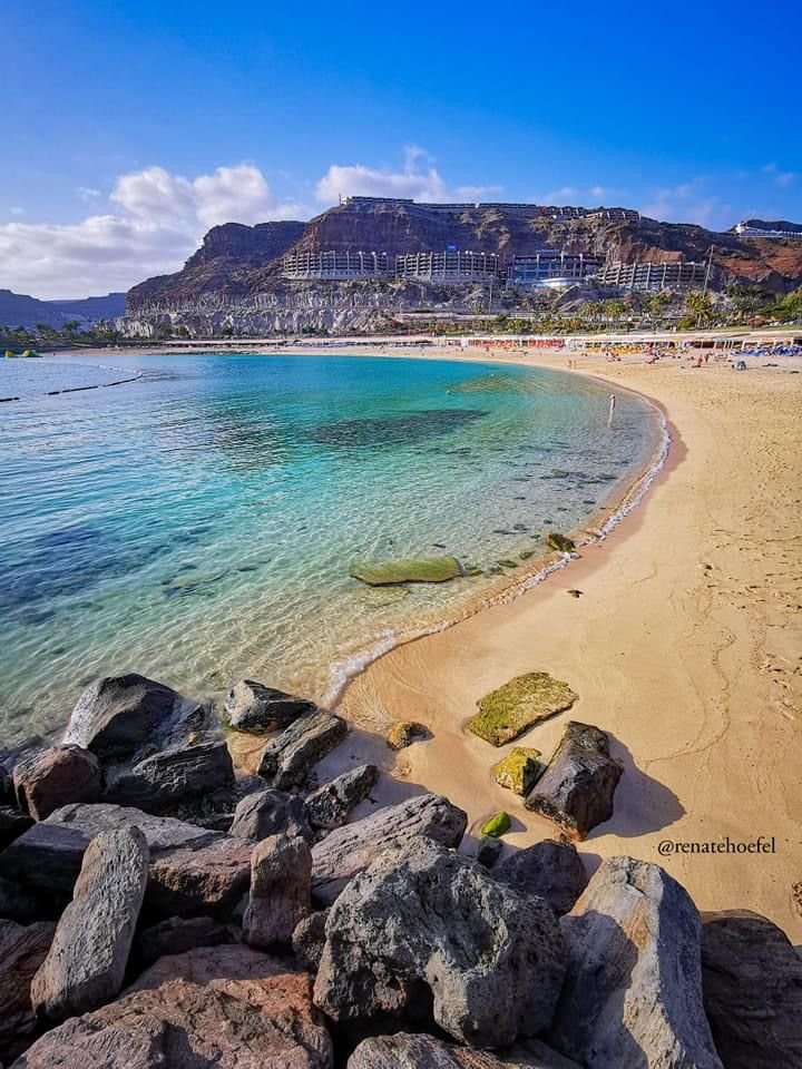 This may contain: a sandy beach with clear blue water and mountains in the background