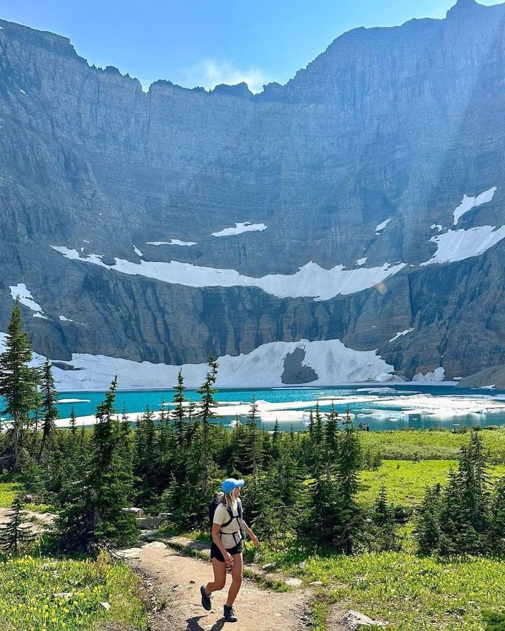 This may contain: a person with a backpack is walking up a trail in front of snow capped mountains