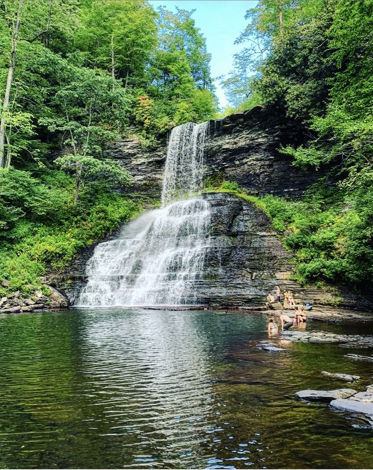 This may contain: people are swimming in the water near a waterfall