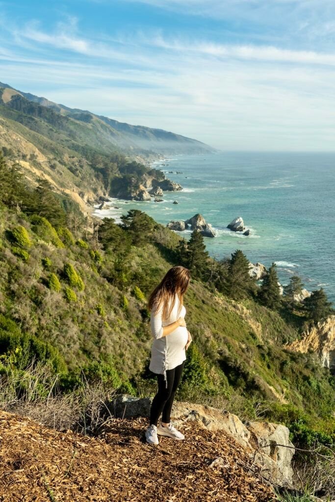 This may contain: a woman standing on top of a hill next to the ocean