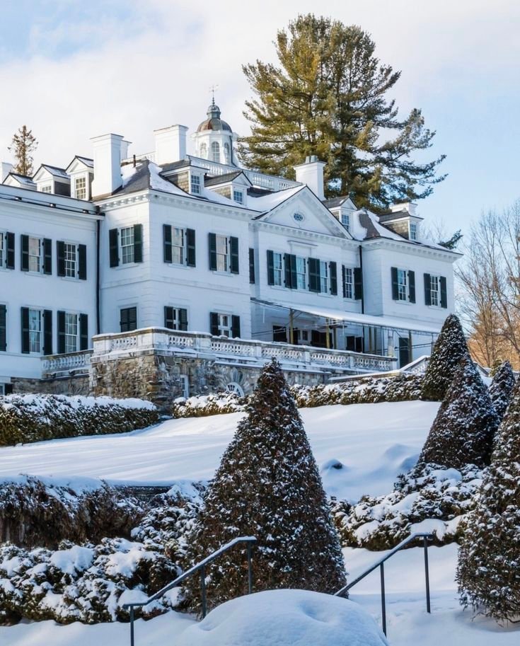 This may contain: a large white house with snow on the ground and trees around it in front of it