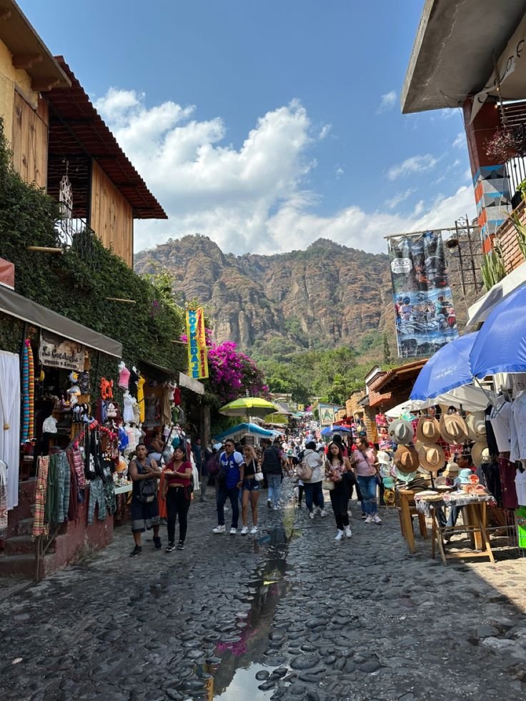 This may contain: people are walking through an open market area with mountains in the backgrouds