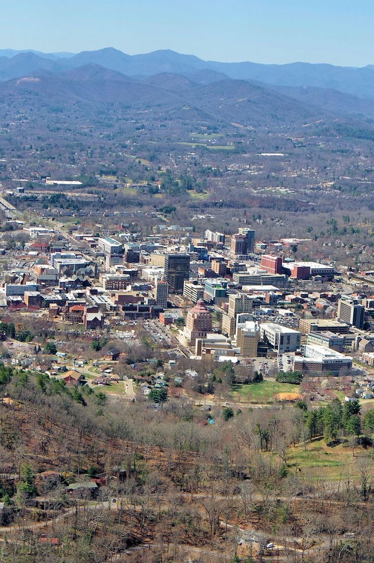 This may contain: an aerial view of a city with mountains in the background and trees on both sides