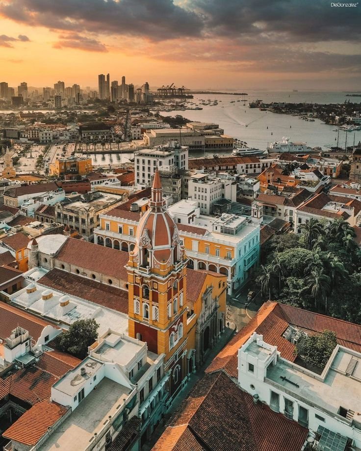 This may contain: an aerial view of a city with tall buildings and water in the background at sunset