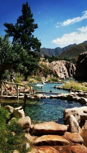 This may contain: people are swimming in a river surrounded by rocks and trees with mountains in the background