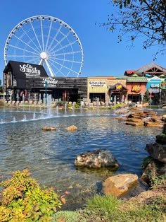 This may contain: an amusement park with a large ferris wheel in the background and water fountains on the ground