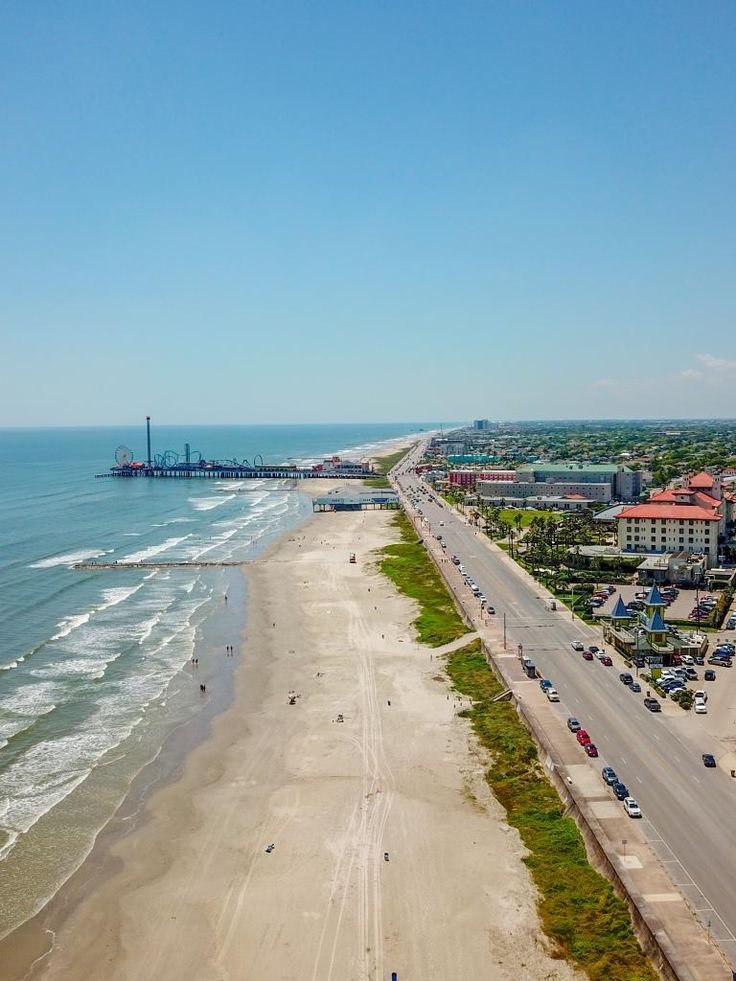 This may contain: an aerial view of the beach and ocean with cars parked on the road next to it