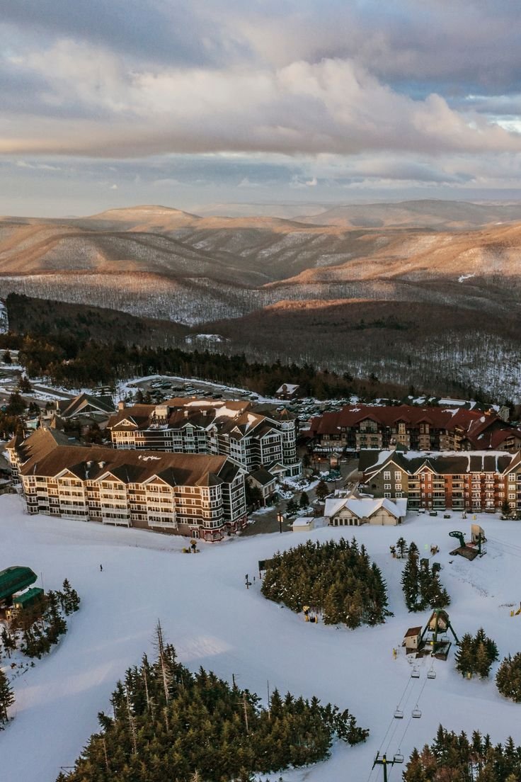 This may contain: an aerial view of a resort surrounded by mountains and trees in the distance is snow - covered ground