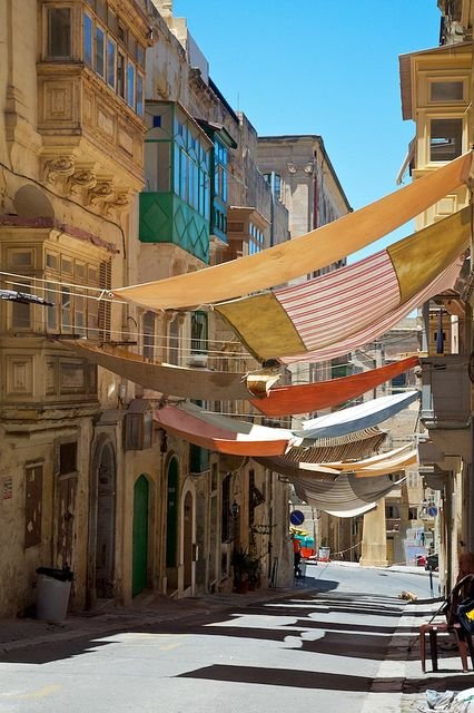 This may contain: an empty city street with lots of flags hanging from the buildings and people sitting on benches