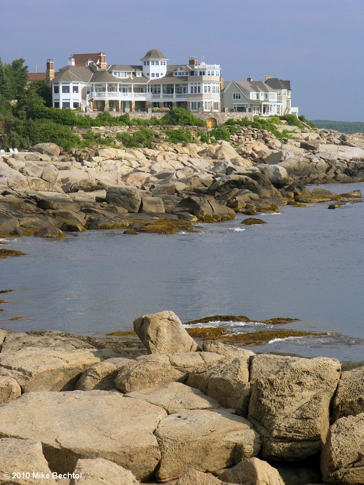 This may contain: a large white house sitting on top of a cliff next to the ocean with rocks in front of it