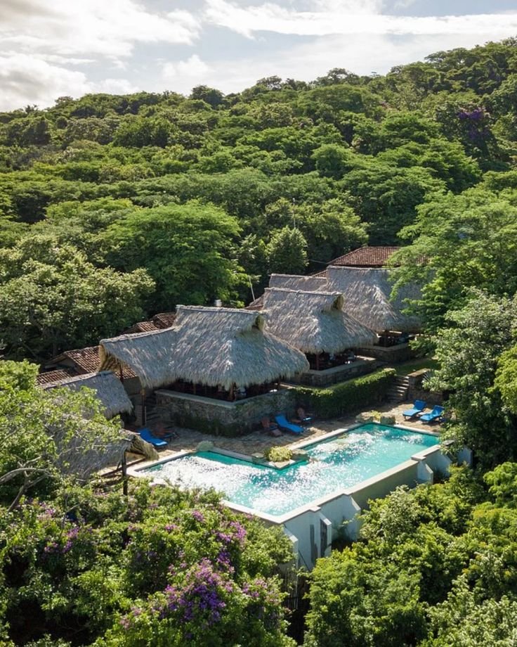 This may contain: an aerial view of a tropical resort surrounded by trees and greenery, with a swimming pool in the foreground