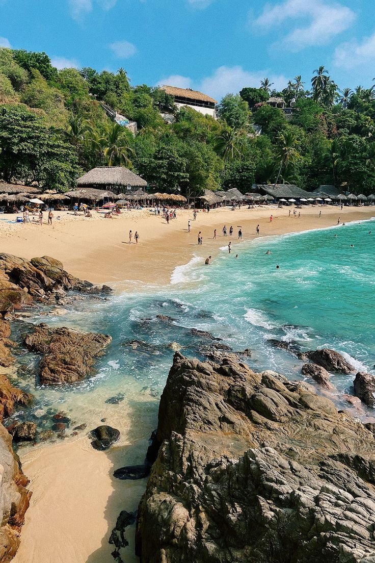 This may contain: people are on the beach and in the water near some rocks with umbrellas over them