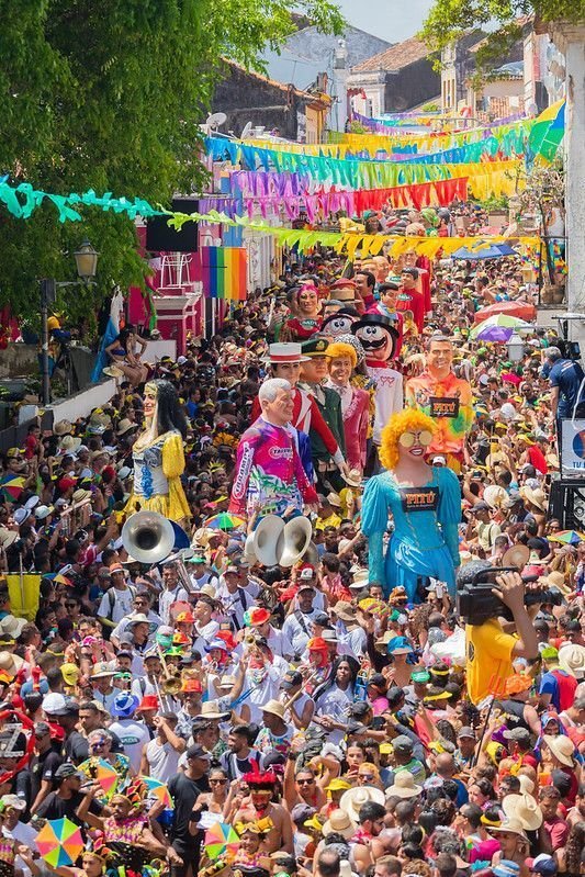 This may contain: a large group of people walking down a street with clowns on the sidelines