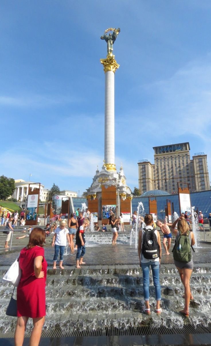 This may contain: many people are walking around in front of a fountain