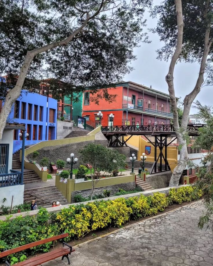 This may contain: a park bench sitting next to trees and colorful buildings on the side of a road