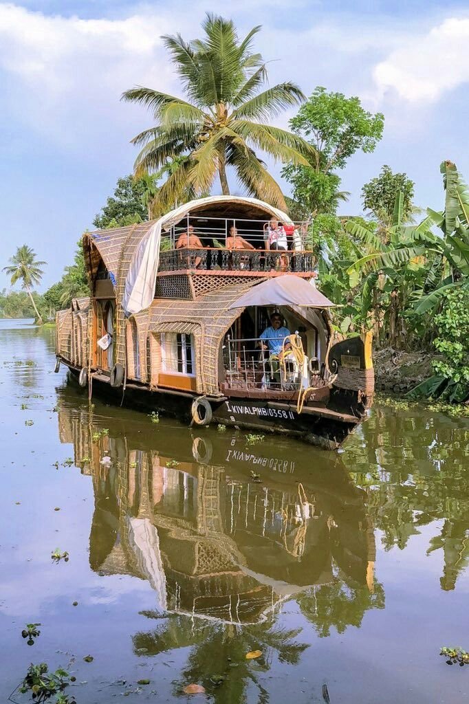This may contain: a house boat with people on it floating down a river surrounded by palm trees and vegetation