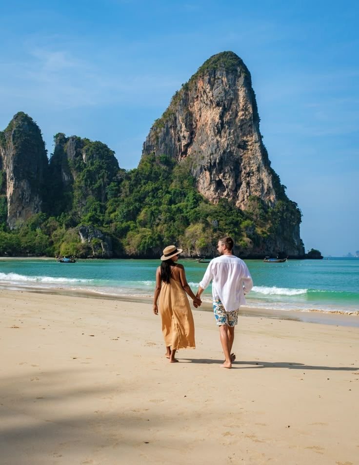 This may contain: a man and woman walking on the beach holding hands