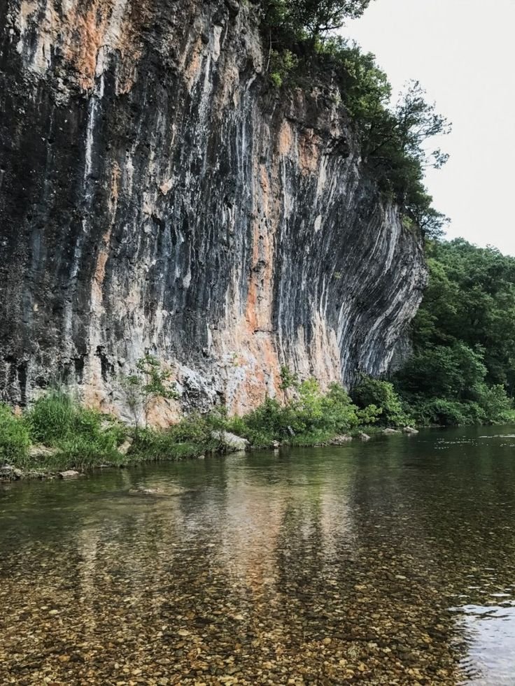 This may contain: the water is crystal clear and there are trees on the side of the cliff next to it