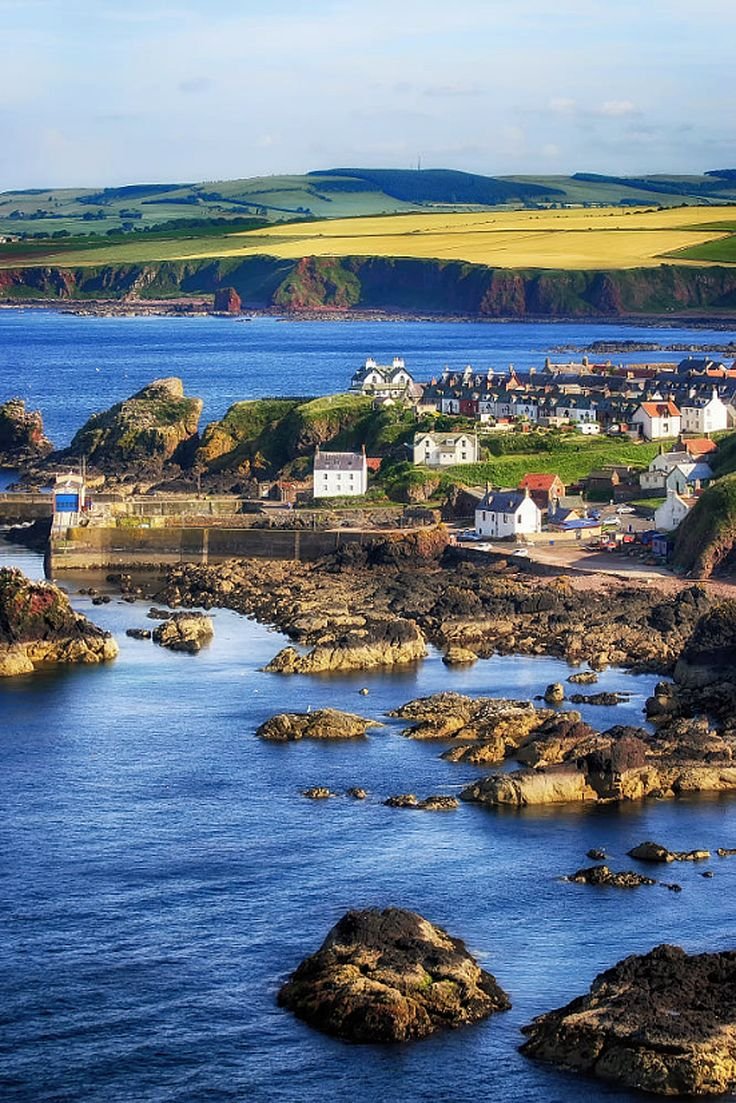This may contain: an aerial view of a small town on the coast with blue water and green hills in the background